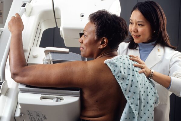 Mulher realizando mamografia de rastreamento acompanhada por profissional de saude