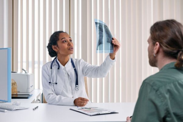 Médica mostra e explica o resultado de um exame de imagem para um paciente no consultório