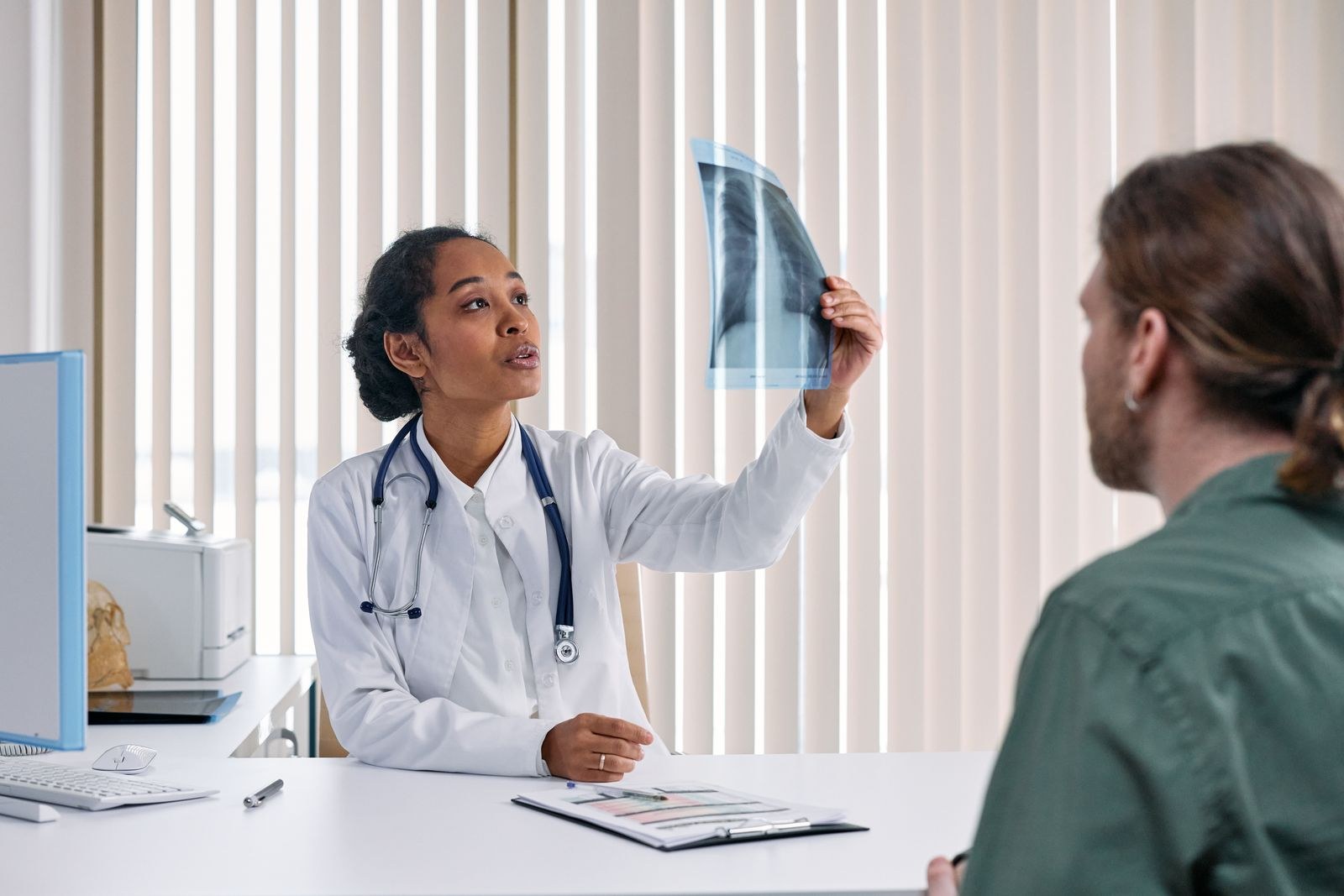 Médica mostra e explica o resultado de um exame de imagem para um paciente no consultório