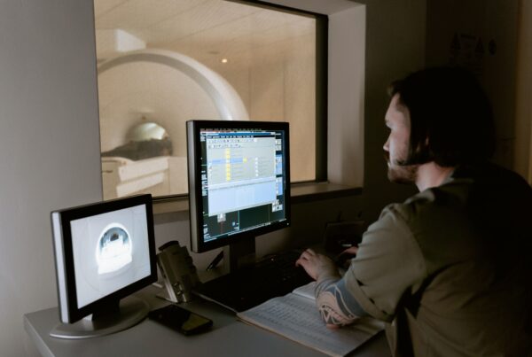 Radiologista avaliando exames de imagem em múltiplos monitores de estação de laudo hospitalar
