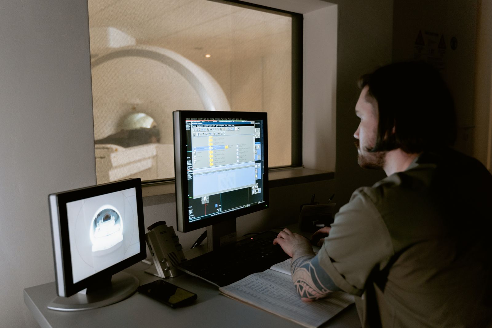 Técnico de resonancia magnética en la consola de la sala de mando mirando hacia la sala del imán
